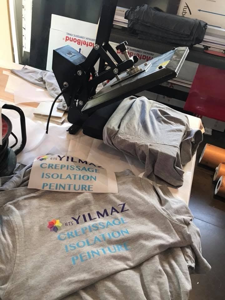 Sweats ETS Yilmaz empilés devant la presse à transfert de l'atelier HM Global